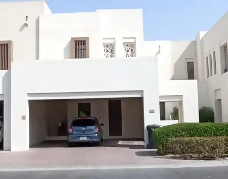 Discover the elegance of a contemporary 3-bedroom villa in Mira Oasis, featuring a sleek white exterior and a covered driveway with a striking blue car parked out front. The upstairs windows are adorned with geometric patterns, adding a touch of sophistication, while neatly trimmed hedges line the inviting entrance. Available for rent through Redlac Real Estate, your trusted partner in Dubais vibrant property market. Experience luxury living at its finest.