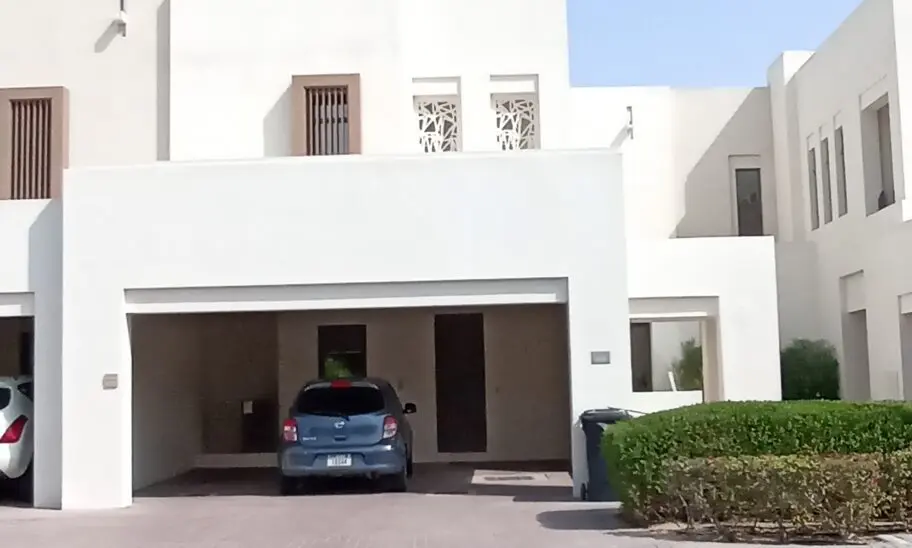 Discover the elegance of a contemporary 3-bedroom villa in Mira Oasis, featuring a sleek white exterior and a covered driveway with a striking blue car parked out front. The upstairs windows are adorned with geometric patterns, adding a touch of sophistication, while neatly trimmed hedges line the inviting entrance. Available for rent through Redlac Real Estate, your trusted partner in Dubais vibrant property market. Experience luxury living at its finest.