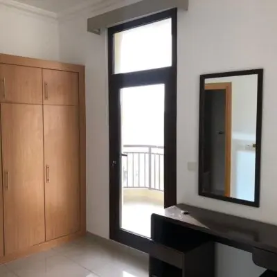 This 1-bedroom apartment showcases a sophisticated design with a wooden wardrobe featuring multiple doors, allowing for ample storage. A large window, complemented by a glass door, opens up to a breezy balcony, inviting plenty of natural light. Inside, youll find a dark desk elegantly topped with a mirror. Nestled in the lively Arjan Dubailand area, this residence boasts tiled floors and immaculate white walls that enhance its spacious feel. Discover premium living spaces like this through Redlac Real Estate in Dubai—where comfort meets style in vibrant communities!.