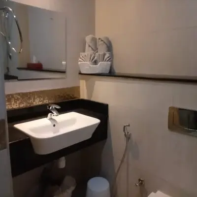 In the image of a contemporary bathroom in a JVC studio apartment, youll find a sleek rectangular sink paired with a stylish wall-mounted faucet. A large mirror hangs gracefully above the sink, enhancing the modern aesthetic. The room is thoughtfully organized with neatly arranged towels and a tissue box on an accessible shelf, and it features the added convenience of a toilet equipped with a bidet. This elegant, efficient space exemplifies Redlac Real Estates commitment to luxurious living in Dubai’s vibrant Jumeirah Village Circle community. Discover your ideal rental haven with Redlac Real Estate today!.