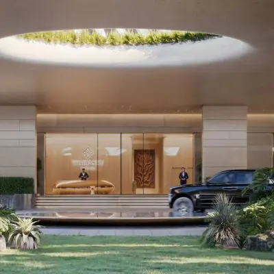 The image captures an elegant hotel entrance featuring a revolving door, accented by two staff members in uniform. This opulence is mirrored in a nearby one-bedroom furnished apartment available for rent in Business Bay. With a sleek black SUV arriving and natural light streaming through the buildings skylight amidst lush greenery, this setting epitomizes luxury living. Explore such refined properties with Redlac Real Estate in Dubai, your gateway to upscale lifestyle opportunities.