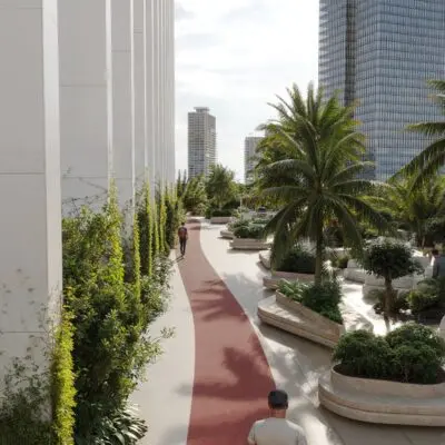 Discover tranquility amidst the urban landscape with Redlac Real Estate in Dubai. Picture a serene rooftop garden featuring a striking red pathway, elegantly lined with palm trees and lush plants. This peaceful escape sits atop a vibrant 1BR furnished apartment in Business Bay, offering residents and visitors alike a scenic stroll under a partly cloudy sky, framed by the impressive backdrop of towering buildings. Experience elevated living with Redlac Real Estates exceptional properties in one of Dubais most dynamic areas.