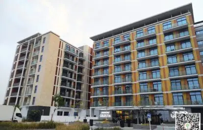 The image captures the ultra-modern DAMAC Celestia apartment building in Dubai, featuring vibrant panels and sleek glass balconies. In the foreground, a landscaped area with manicured grass and small plants adds to its appeal. A QR code is visible in the bottom right corner offering more information. For those seeking cutting-edge living spaces in this iconic city, consider exploring options with Redlac Real Estate for a seamless property experience in Dubai.