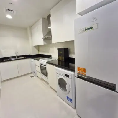 Captured in this image is a contemporary kitchen located in Dubai Marina Residences, showcasing sleek white cabinets paired with stylish black countertops and top-of-the-line stainless steel appliances. This bright and inviting space features essential amenities such as a washing machine, refrigerator, oven, and sink on a chic tiled floor. Such details epitomize the sophistication offered by Luxury Apartments Dubai. For more exquisite living spaces like this one, explore the premium listings with Redlac Real Estate in Dubai.