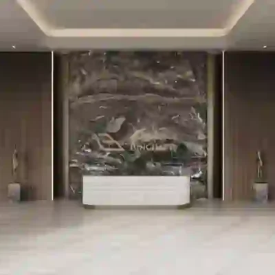 The modern hotel lobby in Dubai Production City showcases a chic white reception desk set against a striking abstract marble art wall. The contemporary decor is enhanced by potted plants and soft lighting, offering breathtaking views that create an inviting and sophisticated ambiance. Explore such stunning properties with Redlac Real Estate in Dubai, where elegance meets modern living.