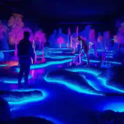 Imagine a group enjoying mini-golf in a vividly lit, neon paradise. Blue pathways glow amidst sleek, modern designs, with pink and purple lights accentuating surrounding plants and structures. This futuristic ambiance melds effortlessly with the lively golf greens. Experience such breathtaking environments by exploring Redlac Real Estate in Dubai, where innovation meets luxury lifestyle in stunning settings.