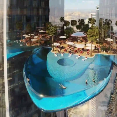 Discover a breathtaking scene: an elevated pool with a glass bottom suspended between two skyscrapers, offering a unique oasis in the sky. Swim and unwind among palm trees and umbrellas while the dazzling cityscape unfolds behind you. This extraordinary spectacle awaits at Safa Two, brought to life by Redlac Real Estate in Dubai—where luxury living meets stunning innovation.