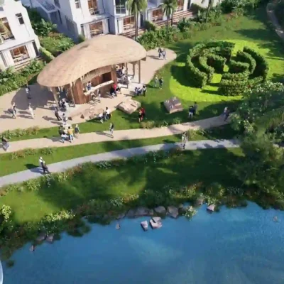 Capture the stunning aerial view of Sun Citys vibrant garden oasis by a tranquil lake. The scene showcases a beautifully designed circular hedge maze, complemented by a charming straw-roofed gazebo and meandering pathways. Visitors leisurely explore this lush haven, with the citys iconic white buildings as a backdrop. Discover similar serene and picturesque living spaces with Redlac Real Estate in Dubai today!.