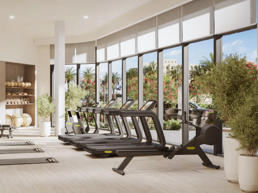 Discover contemporary elegance at a modern gym in Baltimore, boasting expansive windows with views of a lush garden of palm trees and vibrant flowers. Inside, four treadmills rest on gleaming light wood floors, exuding both comfort and sophistication. Conveniently stocked shelves with towels and yoga mats enhance the bright ambiance. Experience this luxury with Redlac Real Estate, your gateway to exquisite properties in Dubai.